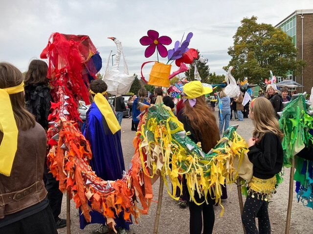A long, brightly coloured dragon puppet made of rags is carried through a crowd at an outdoor parade.